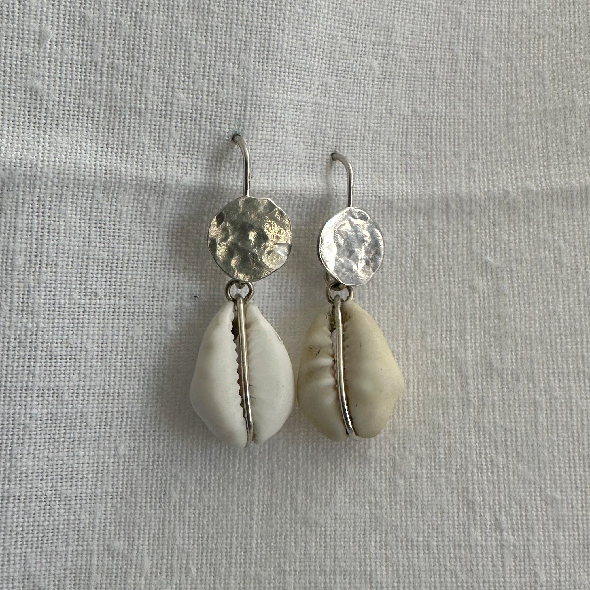 "Détail des boucles d'oreilles cauri Elaheh - texture argent et coquillage naturel"